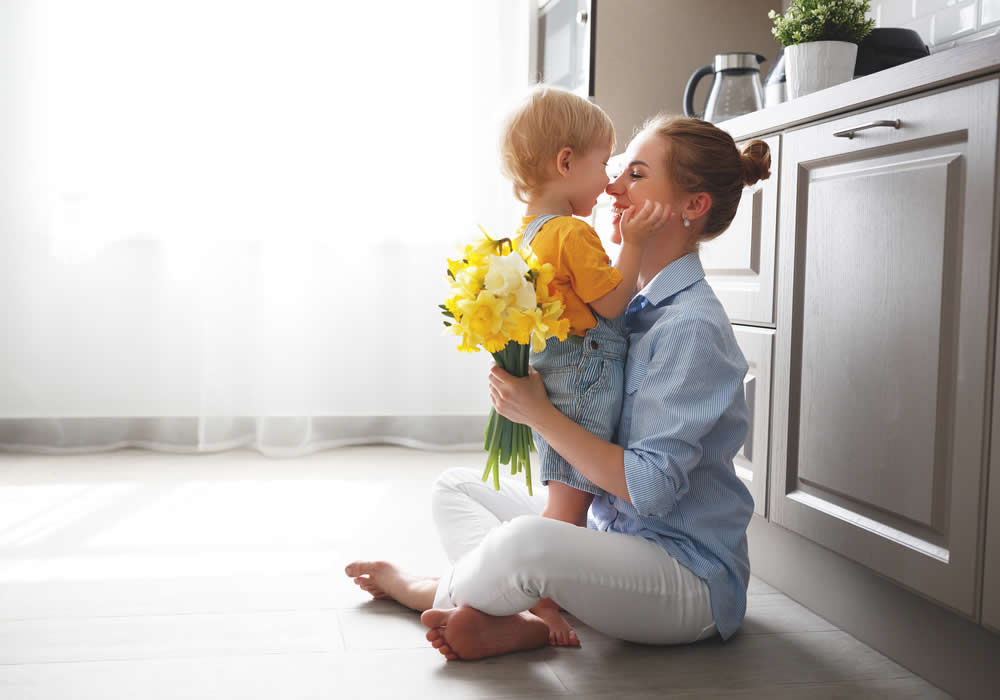 Mother On Floor In Kitchen Holding Flowers Playing With Child