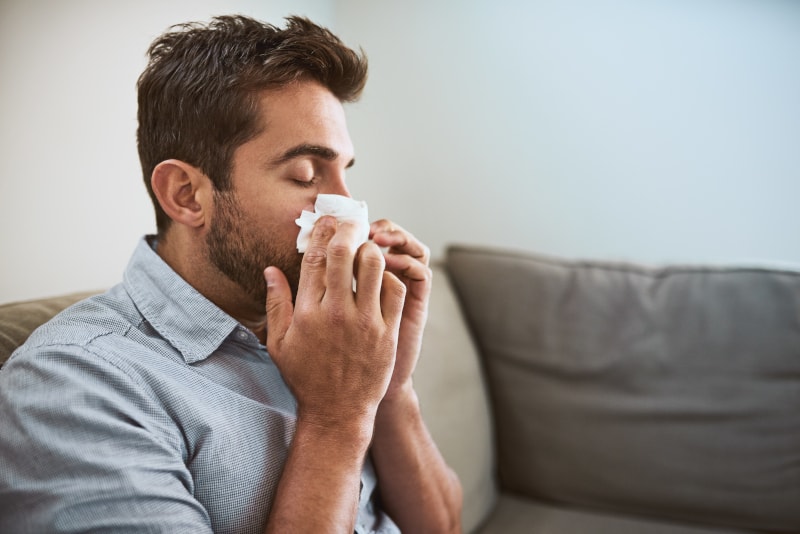 Man Blowing Nose While Sitting On Couch